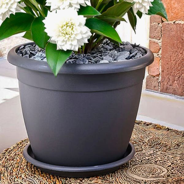 Vaso rotondo Naxos in plastica, vaso con fiori bianchi in balcone su un tappeto.